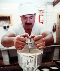 A man in white shirt and hat using a mixer.
