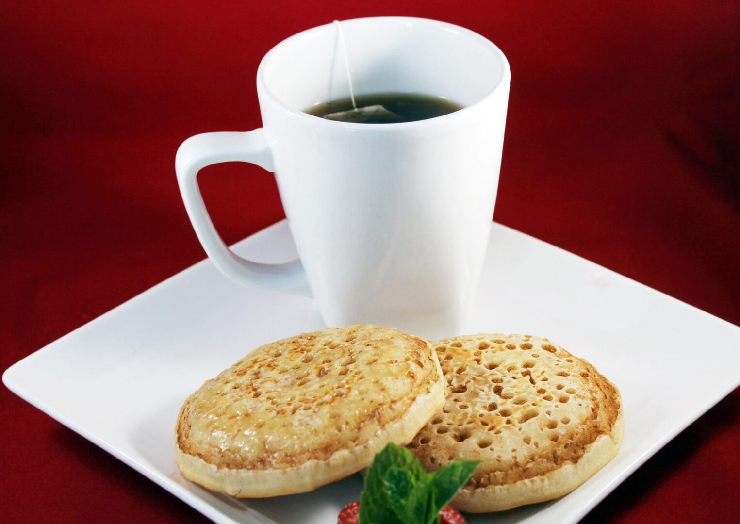 A cup of tea and two english muffins on a plate.